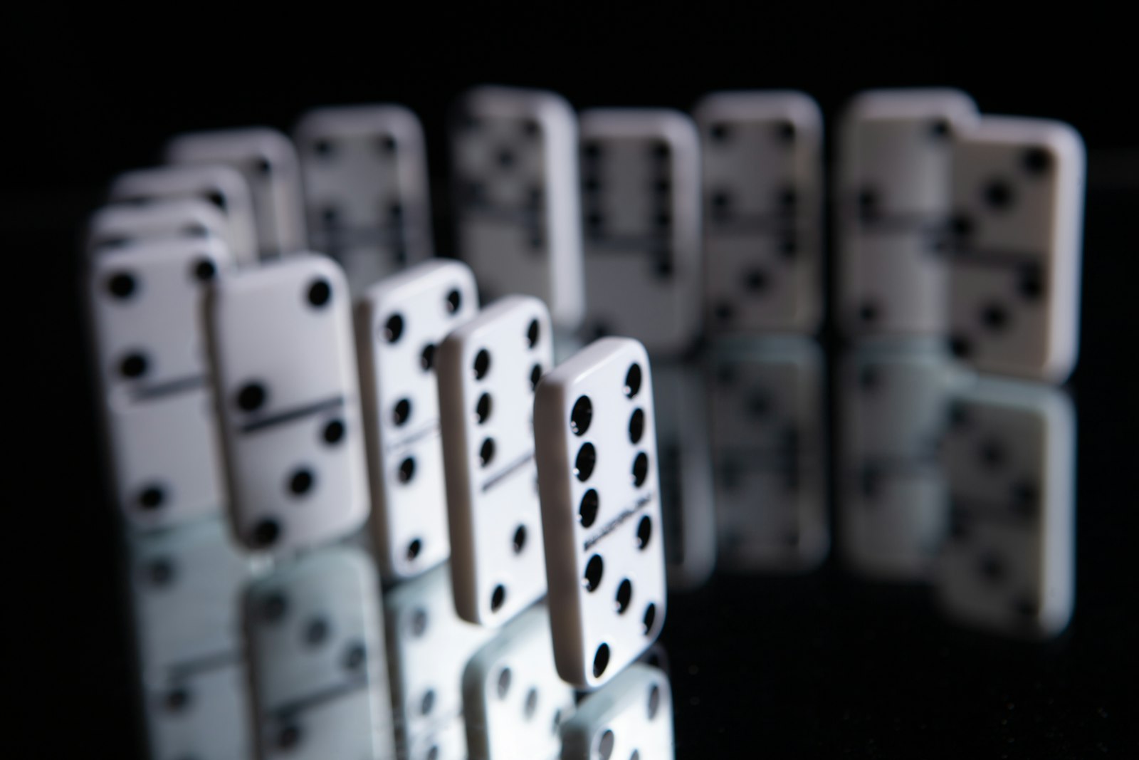 Dominoes standing in a line on a dark reflective surface